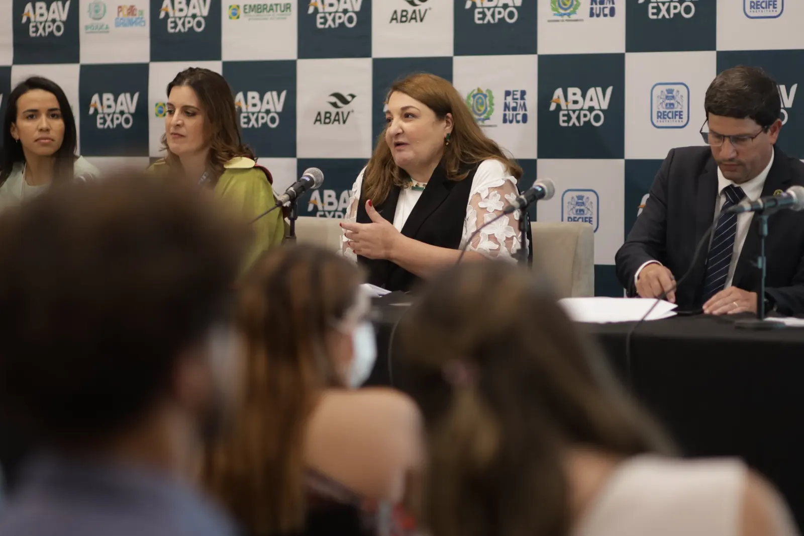 Mesa da coletiva de imprensa da ABAV Expo 2022 diante do painel de patrocinadores