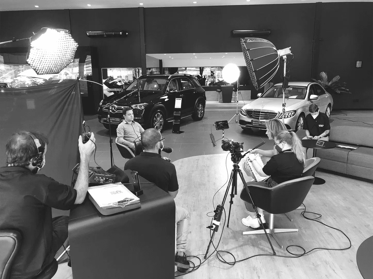 Bastidores em preto e branco de entrevista gravada em concessionária, com luzes e duas câmeras