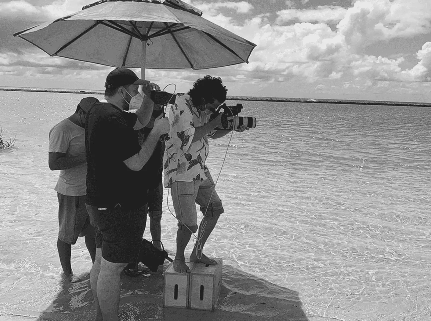 Equipe gravando dentro do mar, com guarda-sol e câmera, em locação de praia