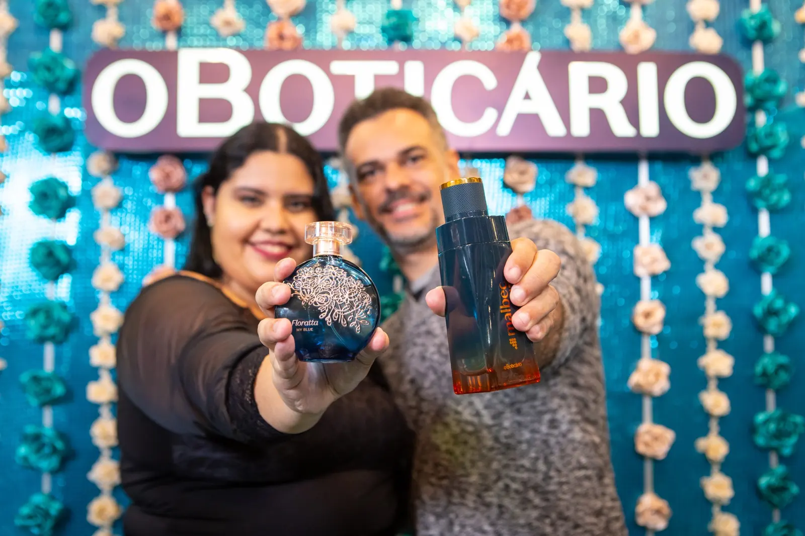 Casal mostrando perfumes Floratta e Malbec no estande de O Boticário